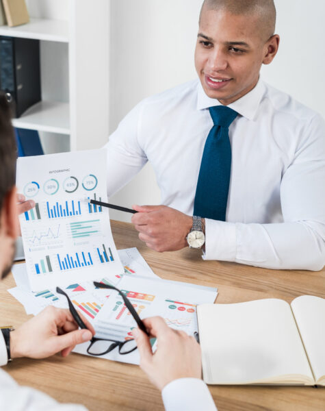 close-up-smiling-young-businessman-showing-graph-with-pencil-his-business-partner-workplace close-up-smiling-young-businessman-showing-graph-with-pencil-his-business-partner-workplace
